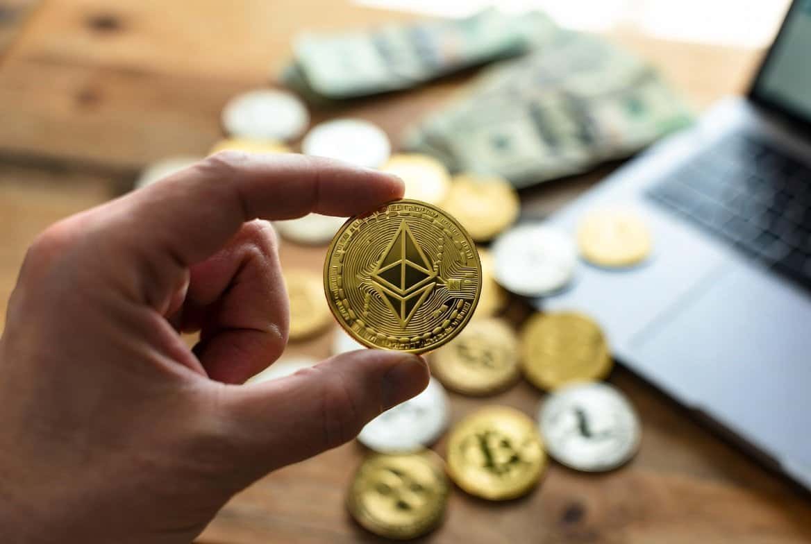 Ethereum gold coin held in hand with scattered crypto coins on desk - ETH price analysis April 2026